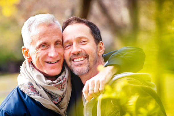 Couple of loving senior gay men portrait in a park in late October Couple of loving senior gay men portrait in a park in late October. They are both in hip mature fashion, happily and closely looking at the camera. gay man stock pictures, royalty-free photos & images