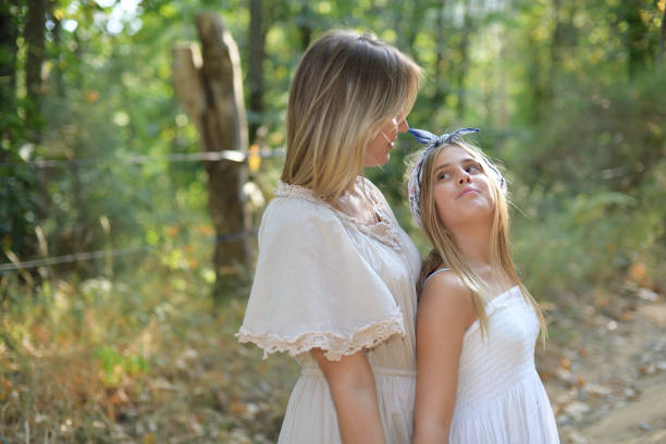 Happy mother and daughter show their affection in a forest in light dresses
