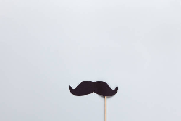 istock Accessory in form of black moustache on stick on grey background with place for text. Concept men's health, prostate cancer awareness month, no shave, charity, Father's Day. Horizontal. Flat lay 1183448358