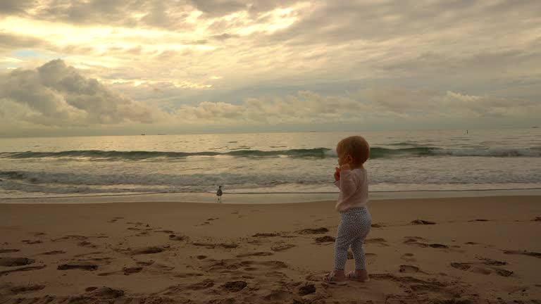 Slow motion video of baby girl plays with her doll on the beach