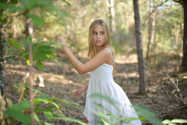 Scared girl running through a forest and looking back in a light dress
