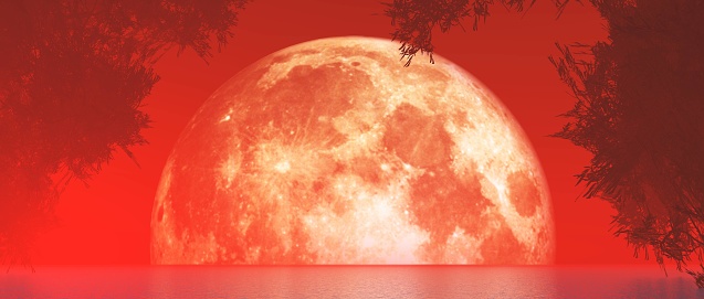 There is a red haze around the moon as it sits low over the lake