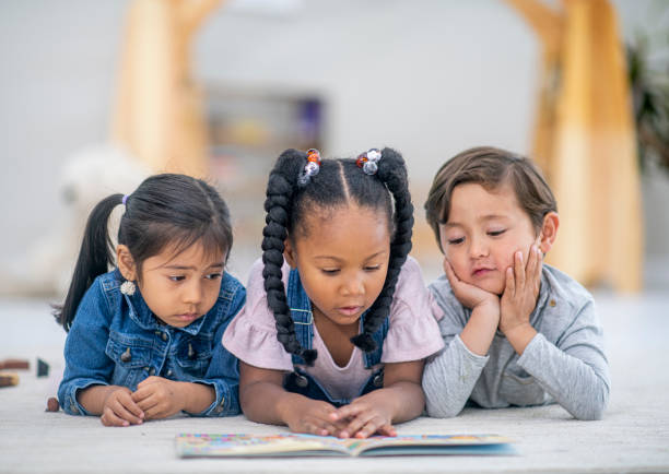 eine gruppe von drei multiethnischen kindern liegen auf dem boden lesen zusammen stockfoto - multi ethnic group reading stock-fotos und bilder