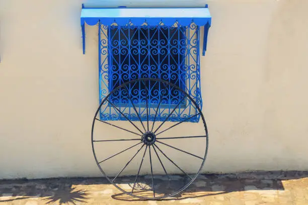 White wall, blue window with lattice ornament and wheel in Sidi Bou Said, Tunisia