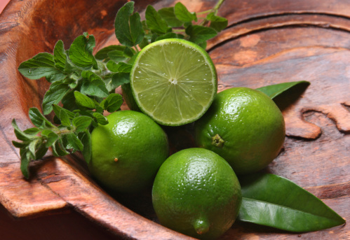 Fresh limes, lime leaves and green herbs on a rustic wooden bowl
