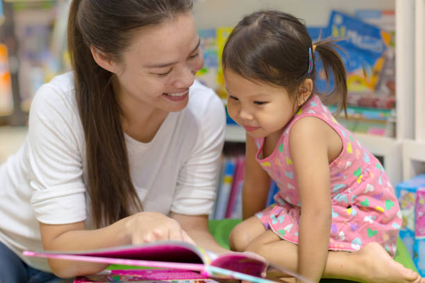 istock Woman reading a book with her child at the library. 1183504119