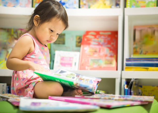 A child reading next to a stack of books. A smart little girl reading books in the bookstore picture book stock pictures, royalty-free photos & images