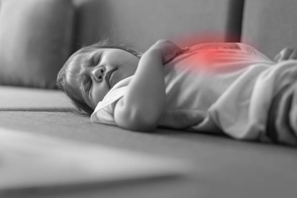 Young child suffering from a painful stomach ache. A small toddler lying on the bed sick, crying from her stomach hurting. Black and white, isolated red. diarrhea photos stock pictures, royalty-free photos & images