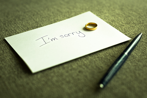 A written paper note text written I'm sorry with a gold wedding ring left on top of it, and pen at home