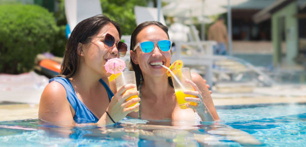 two women drinking cocktails in a pool, on a summer vacation. - summer party drink umbrella concepts imagens e fotografias de stock