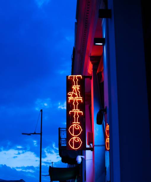 istock Neon lighted banner writing Tattoo against a dramatic blue sky with clouds. 1183508275