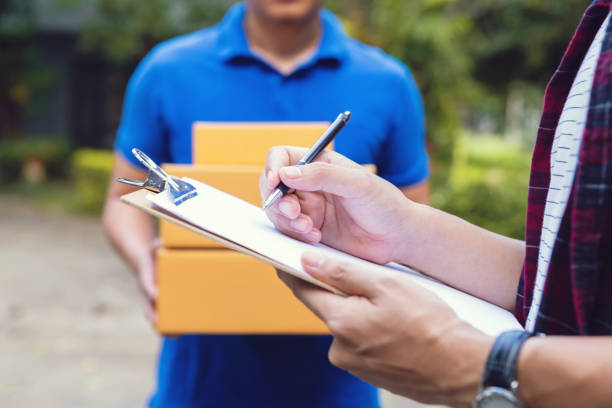 istock Signing to get package. young delivery man holding a cardboard box while beautiful young man putting signature in clipboard 1183515361