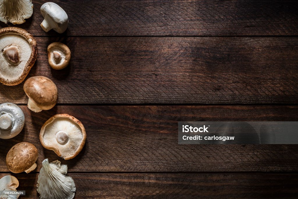 Various kinds of edible mushrooms with copy space Top view of various kinds of edible mushrooms like champignon, shiitake mushroom, oyster mushroom and crimini mushroom on a rustic wooden table. The mushrooms are at the left border of the image so there is a useful copy space at the right side. Low key DSLR photo taken with Canon EOS 6D Mark II and Canon EF 24-105 mm f/4L Mushroom Stock Photo