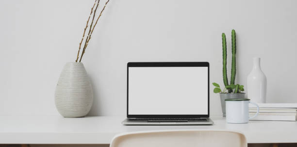 istock Minimal workspace with open laptop computer and decorations on white table and white wall 1183533639