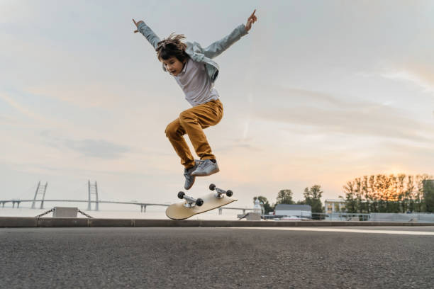 junge springt auf skateboard auf der straße. - skateboardfahren stock-fotos und bilder