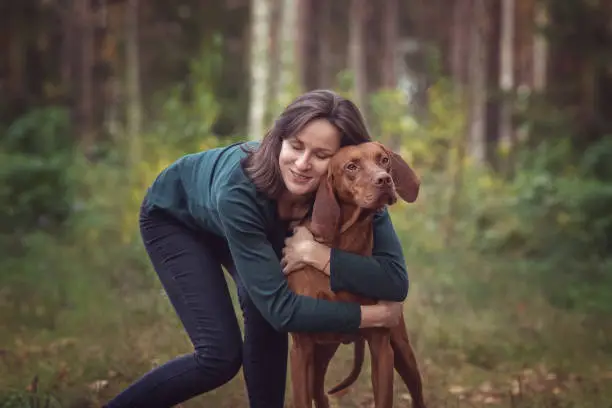 Happy young woman having fun with a hungarian viszla dog during a walk in the autumn forest