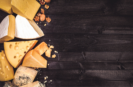 Various types of cheese on black wooden background with copy space. Cheddar, parmesan, emmental, blu cheese. Top view, photo filtered in vintage style