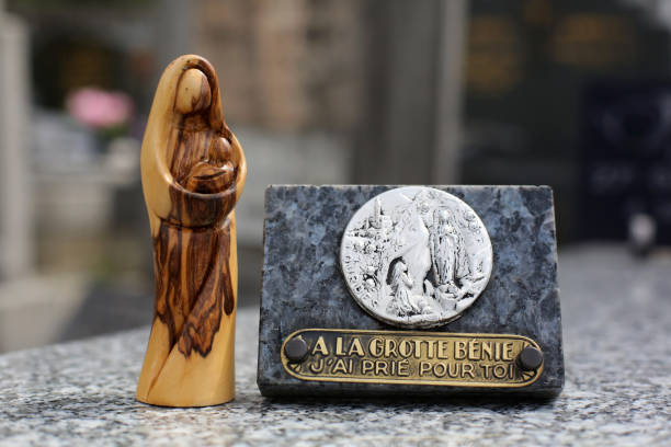 France. April, 26, 2019. Statue of the Virgin and Child in olive wood placed on a tombstone and close to a commemorative plaque composed of an inscription: to the cave bless, I prayed for you. France. April, 26, 2019. The color image depicts a statue of the Virgin and Child in olive wood placed on a tombstone and close to a commemorative plaque composed of an inscription: to the cave bless, I prayed for you. place of burial stock pictures, royalty-free photos & images