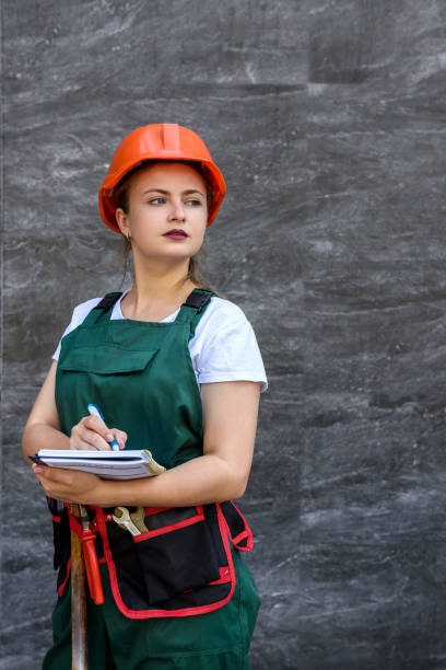 istock Woman worker in coverall with tool belt posing near grey wall 1183556531