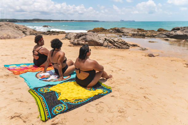 Rear view of women sitting in beach sarong Women, Tourists, Beach, Rear View, Summer black woman bathing suit stock pictures, royalty-free photos & images