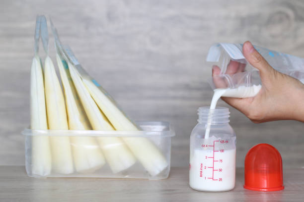 woman pouring milk in to bottles for new baby on wooden table woman pouring milk in to bottles for new baby on wooden table breast milk stock pictures, royalty-free photos & images