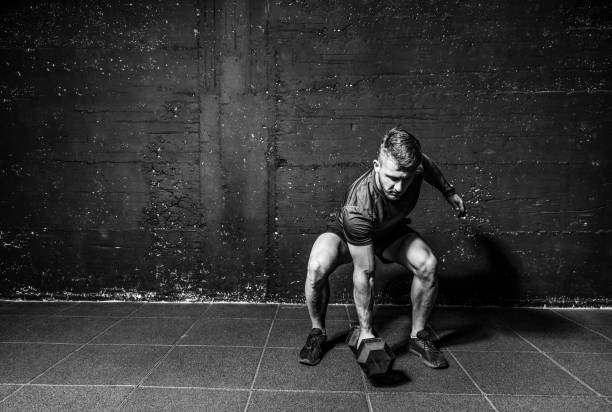istock Young strong fit muscular sweaty man with big muscles strength cross workout training with dumbbells weights in the gym dark image with shadows real people black and white 1183582003