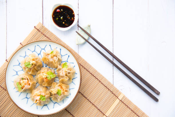 cocina gastronómica cantonesa dimsum. gambas frescas envueltas en albóndigas amarillas, china al vapor envuelta en dumplings amarillo.fondo de suelo de madera blanca, espacio. comida dim sum popular china. - shumai fotografías e imágenes de stock