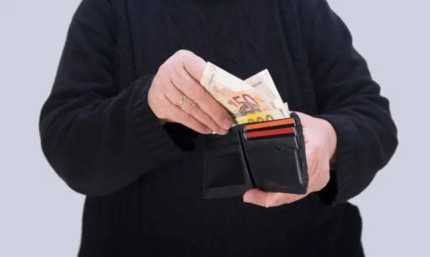 Midsection of an unrecognizable senior adult getting Euro banknotes from wallet on a gray background. Horizontal composition, studio shot.