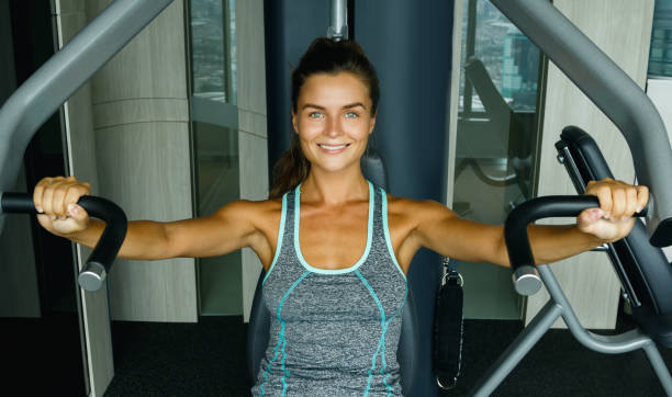 mujer usando máquina de prensa en el gimnasio - body building determination deltoid wellbeing fotografías e imágenes de stock