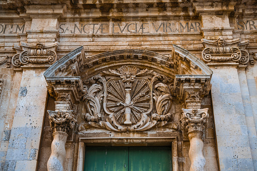 Old wooden church door with the decorative carving above in the main square of the island Ortigia in Siracusa, Sicily, south Italy