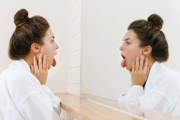 Woman looking on her tongue in the mirror Young woman is looking on her tongue in the mirror sticking out tongue photos stock pictures, royalty-free photos & images