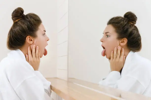 Photo of Woman looking on her tongue in the mirror