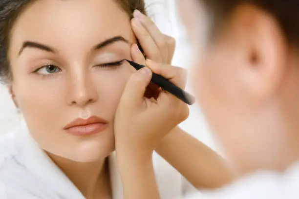 Young woman is applying eyeliner