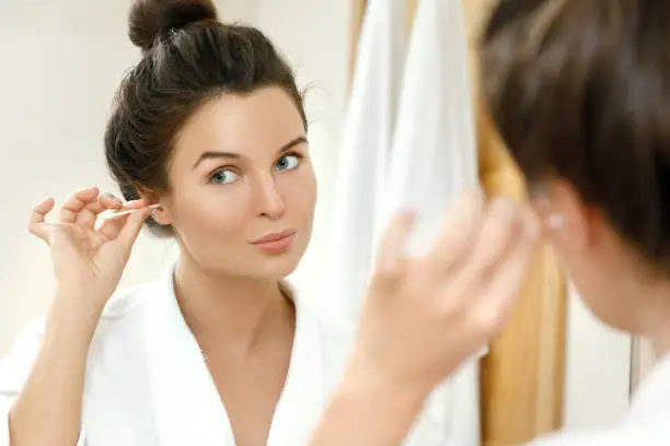 Woman cleansing her ears with a cotton swab in the bathroom