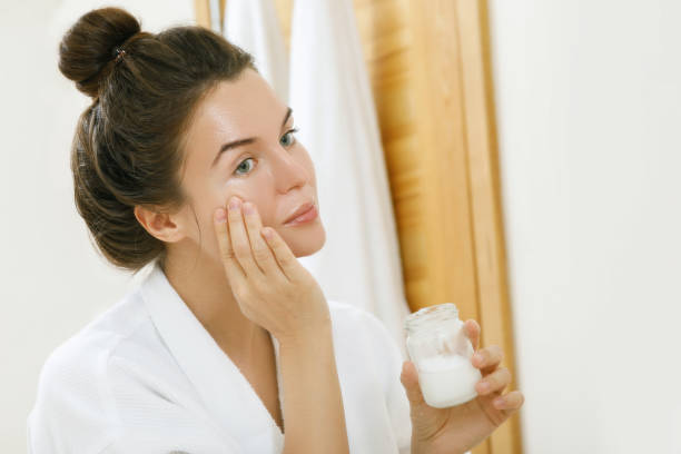 женщина применения кокосового масла на ее лице - moisturizer beauty treatment human skin applying стоковые фото и изображения