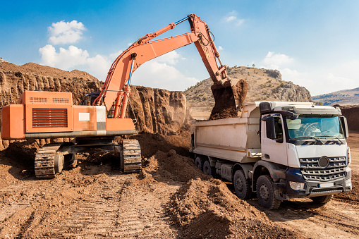 Excavator loading dumper trucks at sunset