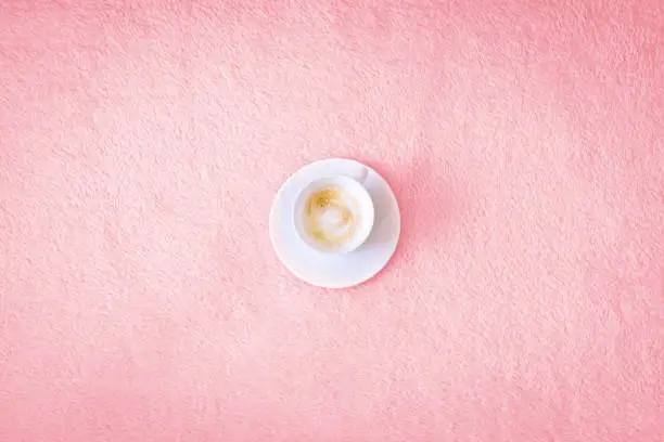 Photo of Cup of coffee on a pink background. A cappuccino in a white cup is centered on a pink bedspread or rug