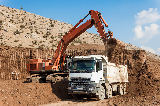 Excavator loading dumper trucks at sunset