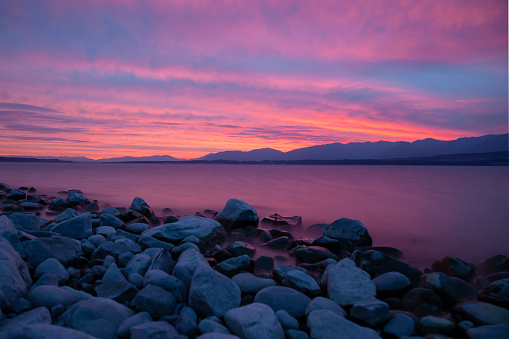 Sunset at Lake Tekapo, New Zealand. Some scattered clouds beeing illuminated in vibrant red, purple and orange colors from the setting sun.