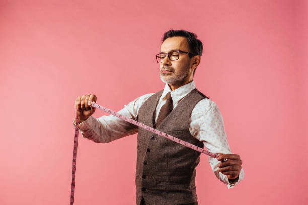 Portrait of a tailor looking down at fabric measure, isolated on pink studio background
