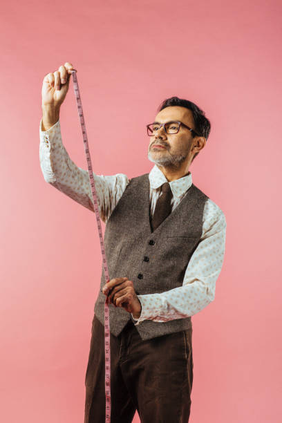 vertical portrait of a tailor holding fabric measure, isolated on pink studio background - made man object imagens e fotografias de stock