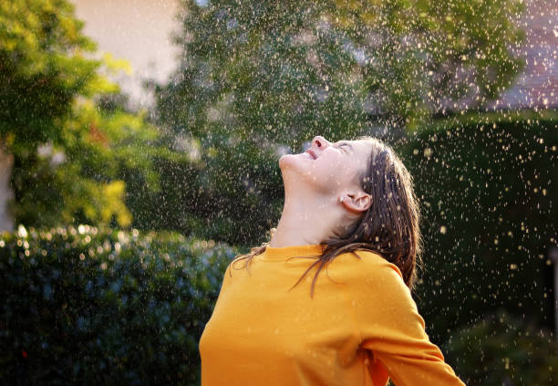 Happy cheerful teenage girl enjoying rain and sun putting her face under water drops smiling happily. True happiness. Summer lifestyle. stock photo