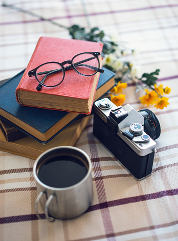 Stack of books, cup of coffee, glasses and a SLR camera on the bed, daylight shot, selective focus