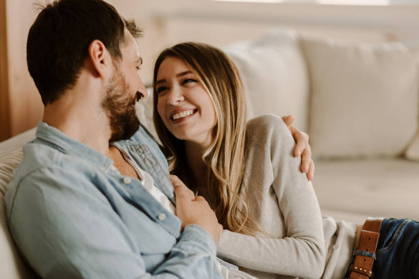 couples heureux détendant à la maison et regardant l'un l'autre - tomber amoureux photos et images de collection