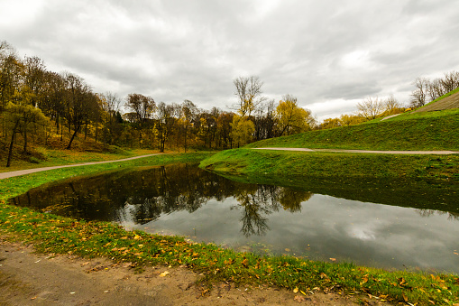 river in the autumn city park. road, green grass and yellow leaves in autumn park
