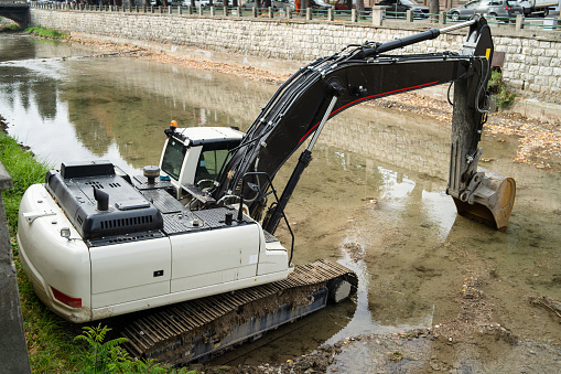 White excavator in the river cleaning the riverbed water course