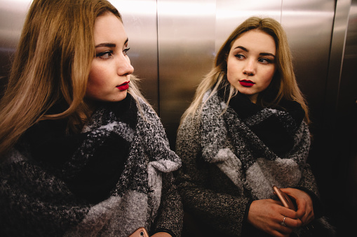 Young woman in warm clothing looking in the mirror in the elevator