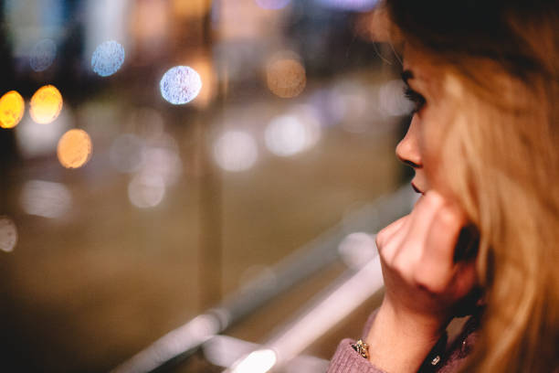 istock Young woman looking through window at night 1183623370