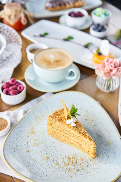 Honey sponge cake decorated with meringue and mint leaves.. Breakfast in the cafe, morning coffee. Cappuccino and lots of desserts on the table.