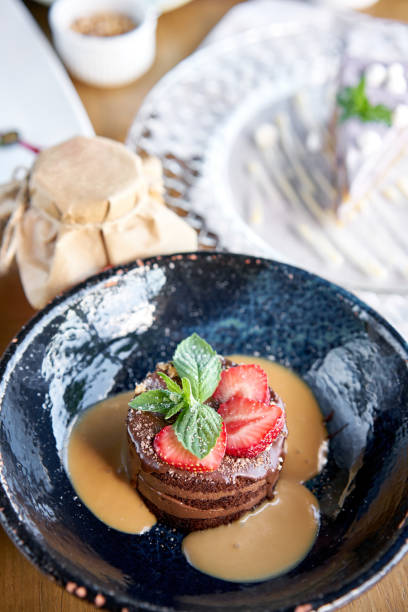 istock Chocolate sponge cake, with caramel, decorated with strawberries and mint leaf. Breakfast in the cafe, morning coffee. Cappuccino and lots of desserts on the table. 1183637886